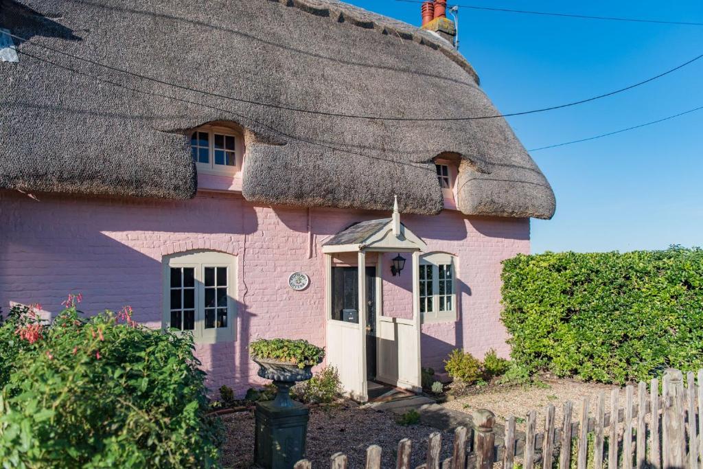 a pink house with a thatched roof at Raspberry Cottage by Bloom Stays in Great Mongeham