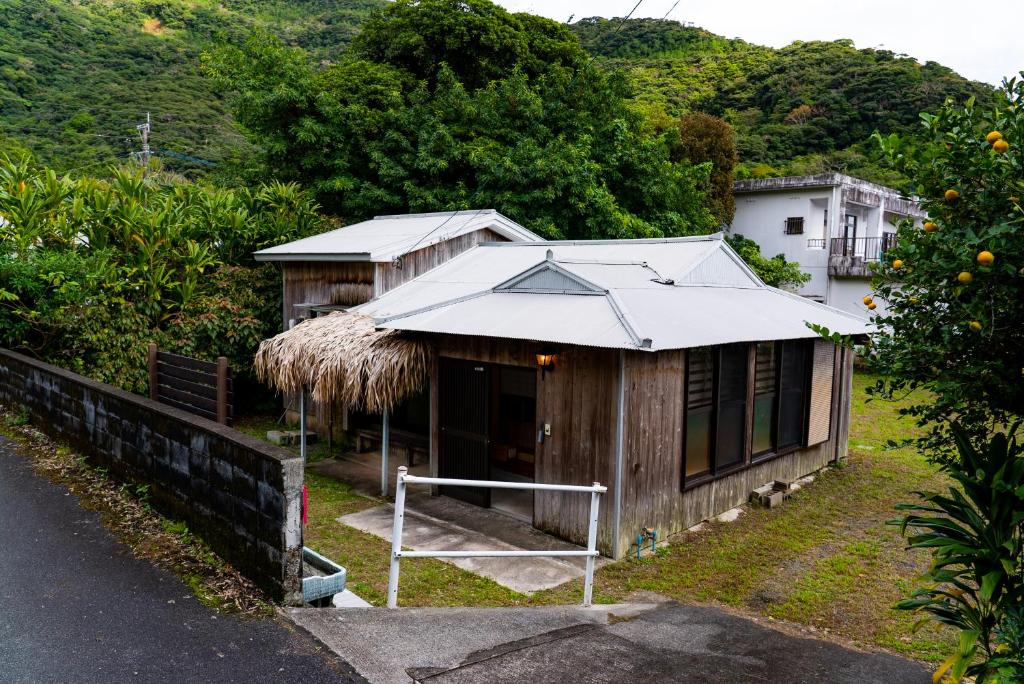 une petite maison avec un toit en paille sur le côté d'une route dans l'établissement ゲストハウス ハルの家, à Amami