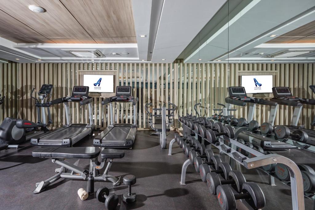 A mirrored fitness room equipped with treadmills, exercise bikes, dumbbells, and benches.