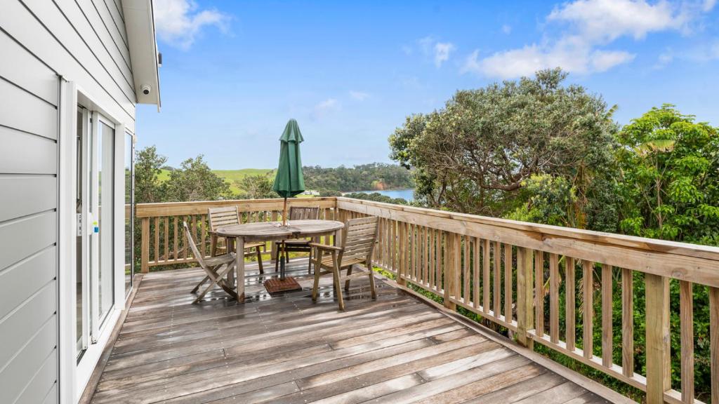 a deck with a table and chairs and an umbrella at Pohutukawa Paradise - Martins Bay Holiday Home in Mullet Point