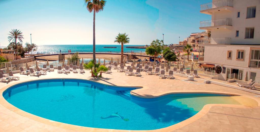 una piscina con sedie e l'oceano sullo sfondo di Apartamentos Playa Moreia a S'Illot