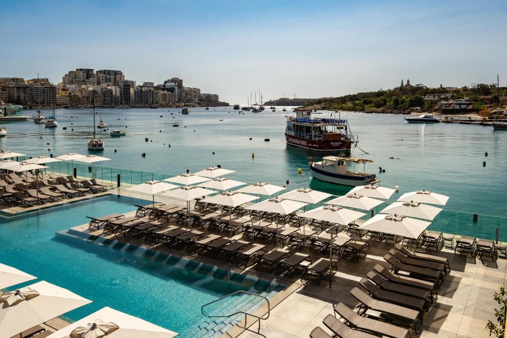 a pool with chairs and boats in the water at 115 The Strand Hotel by NEU Collective in Il-Gżira