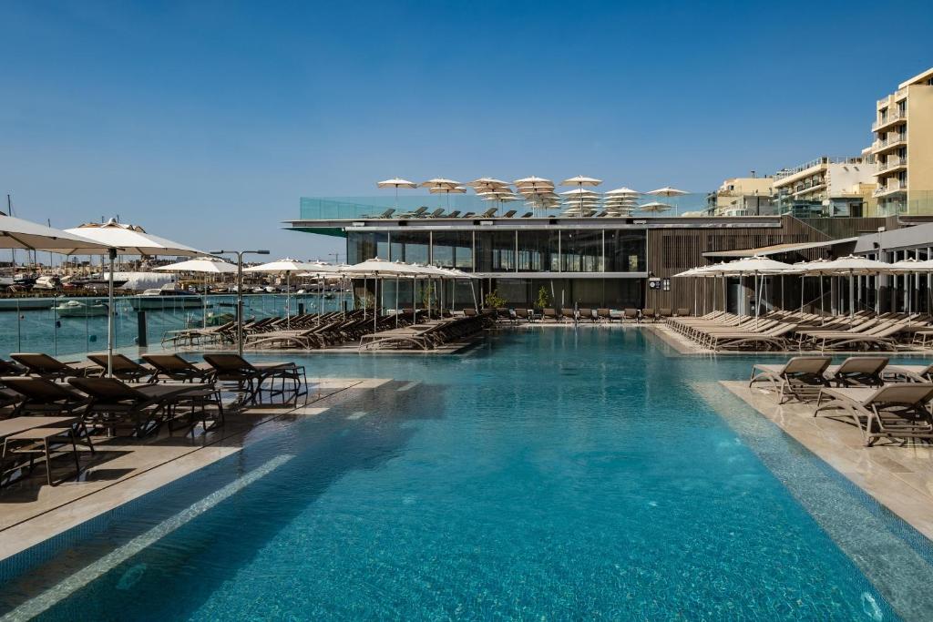 a swimming pool with chairs and umbrellas on a building at 115 The Strand Hotel by NEU Collective in Il-Gżira