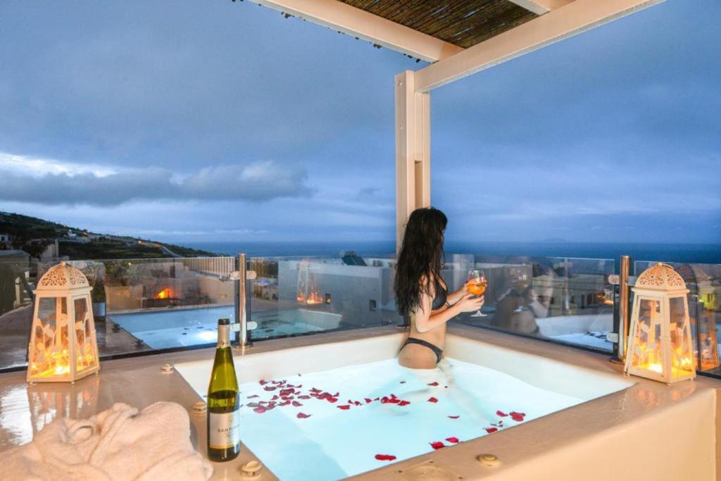 una mujer sentada en una bañera de hidromasaje en el balcón de un edificio en Suite Home Santorini, en Fira