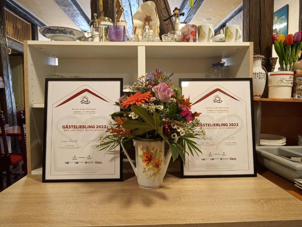 tres certificados enmarcados en una mesa con un jarrón de flores en Pension an der Stadtmauer Apartments, en Wernigerode