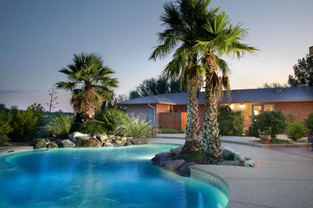 a swimming pool with palm trees in front of a house at Cactus Cove Bed and Breakfast Inn in Tucson