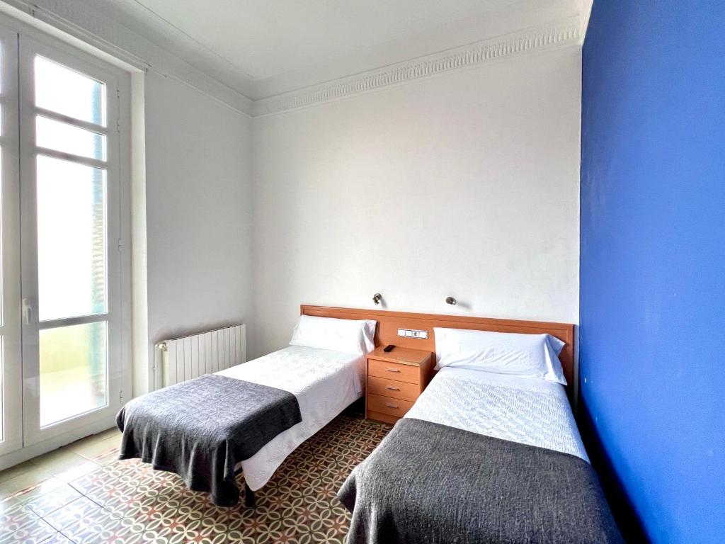 2 camas en una habitación con una pared azul en Pensión Peiró, en Barcelona