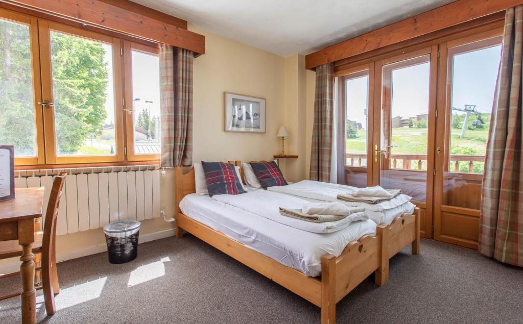 a bedroom with a bed and a desk and windows at Hotel Le Chamois in L&#39;Alpe-d&#39;Huez