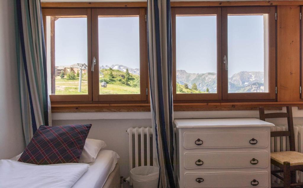 a bedroom with three windows and a bed and a dresser at Hotel Le Chamois in L&#39;Alpe-d&#39;Huez