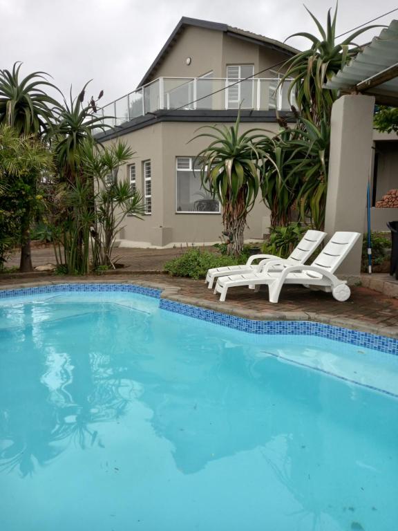 uma piscina com duas espreguiçadeiras e uma casa em Dolphin Den em Port Shepstone