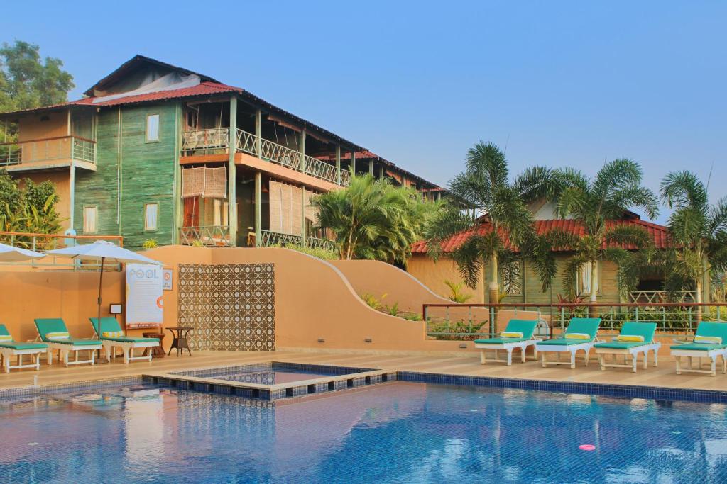 um resort com uma piscina e cadeiras e um edifício em Oxygen Resorts Morjim, Goa em Morjim