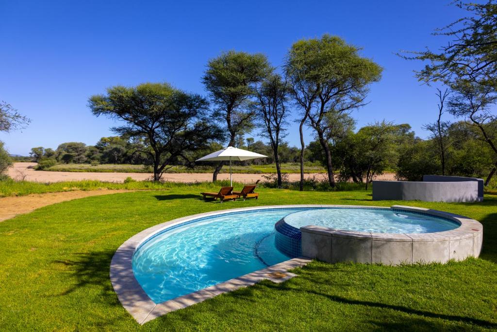 a pool in the grass with a bench and an umbrella at TimBila Camp Namibia in Omaruru