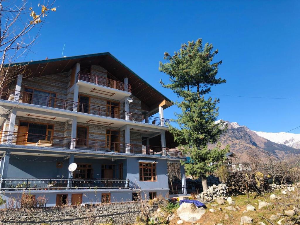 a large building with a tree in front of it at Prāṇa Boutique Stays in Vashisht