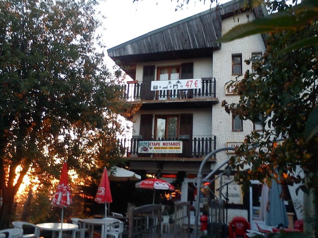 ein Gebäude mit einem Balkon, Tischen und Sonnenschirmen in der Unterkunft Hôtel Les Chamois in La Bollène-Vésubie