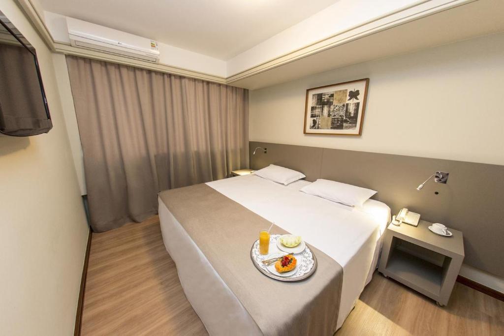 a hotel room with a bed with a plate of food on it at Alta Reggia Plaza Hotel in Curitiba