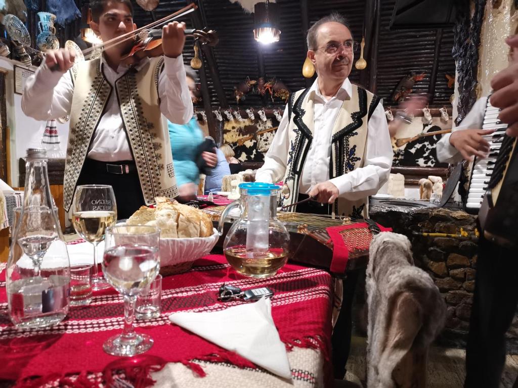 zwei Männer spielen Instrumente an einem Tisch mit Weingläsern in der Unterkunft Cabana Fantanita cu Brazi in Poiana Brașov