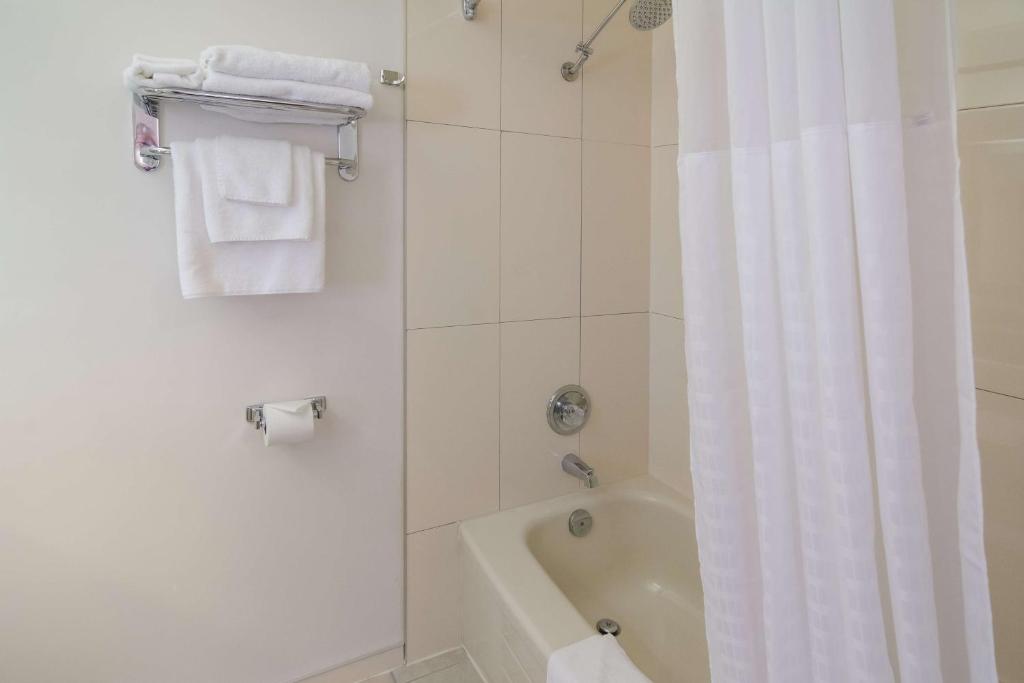 a bathroom with a tub and a shower with a white shower curtain at SureStay Hotel by Best Western North Vancouver Capilano in North Vancouver