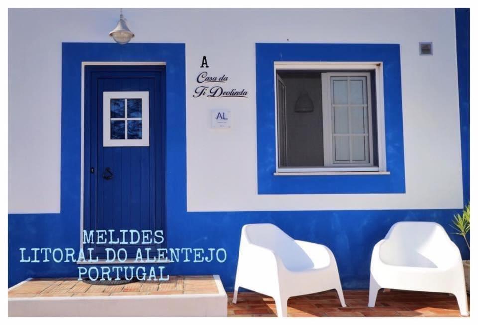 two white chairs in front of a blue wall with a door at A Casa da Ti Deolinda in Melides