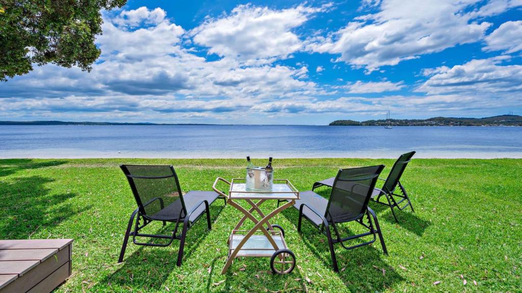 una mesa y cuatro sillas en un campo con agua en Footprints on Foreshore, en Salamander Bay