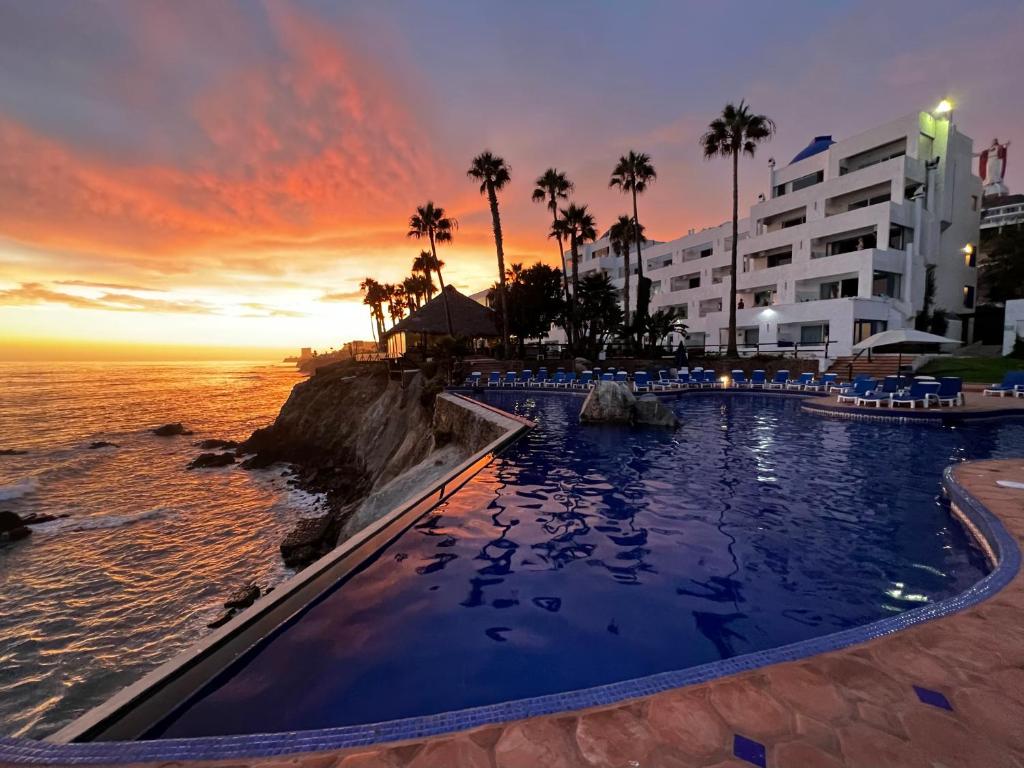 a pool at the beach with a sunset in the background at Las Rocas Resort & Spa in Rosarito