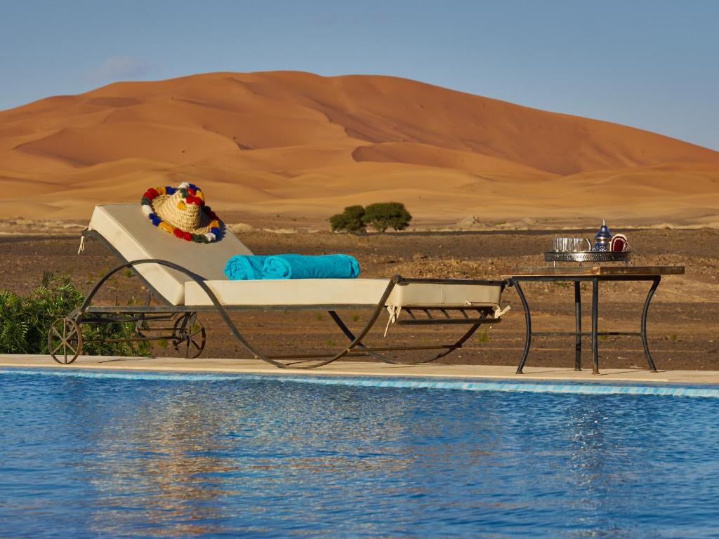 una cama y una mesa junto a una piscina en un desierto en Riad Madu en Merzouga