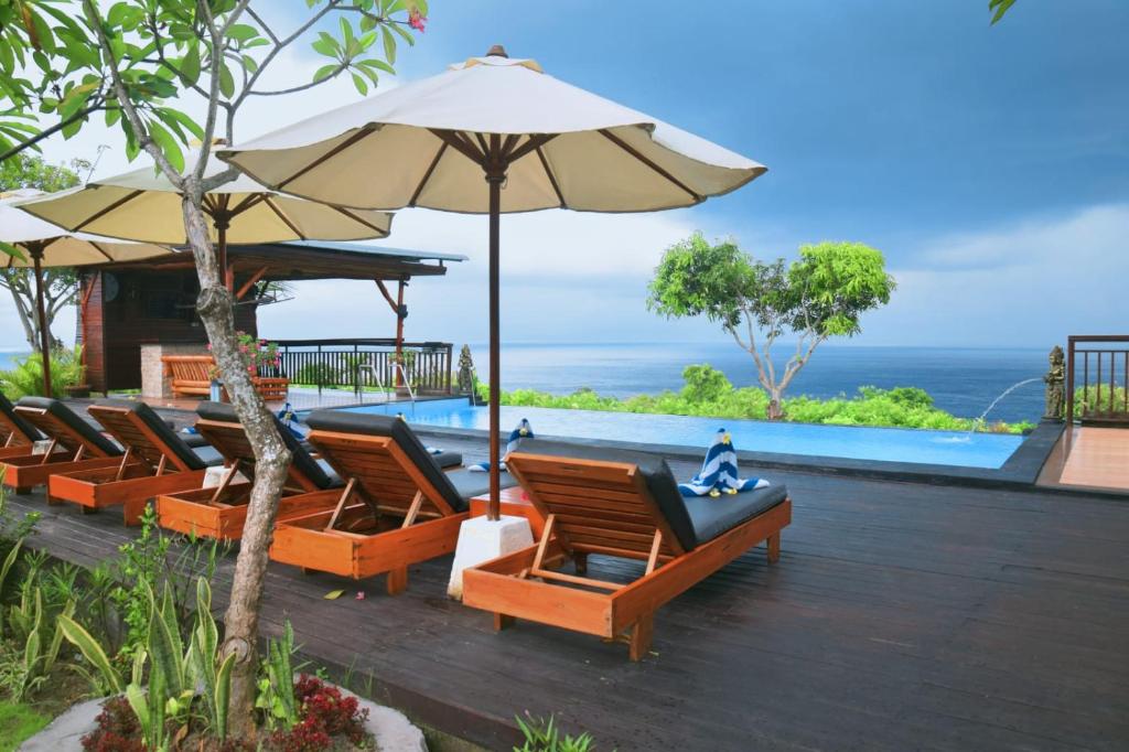 a row of chairs and an umbrella next to a pool at Bataran Garden Cottage in Nusa Penida