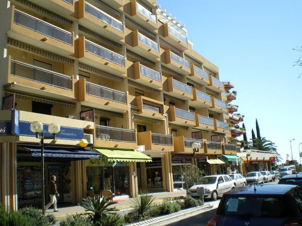 un grand bâtiment jaune avec des voitures garées devant lui dans l'établissement Joli Appartement au Lavandou Centre - 2 Chambres, Terrasse Sud et Garage - FR-1-308-109, au Lavandou