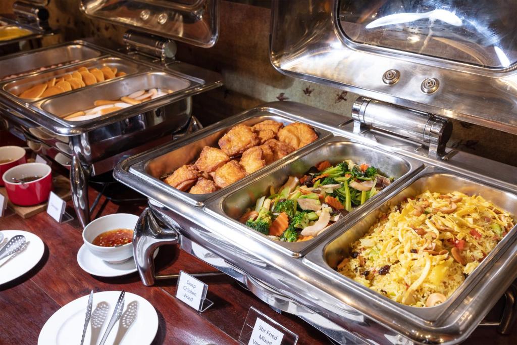 A buffet line with rice, vegetables, fried items, sausages and bread.