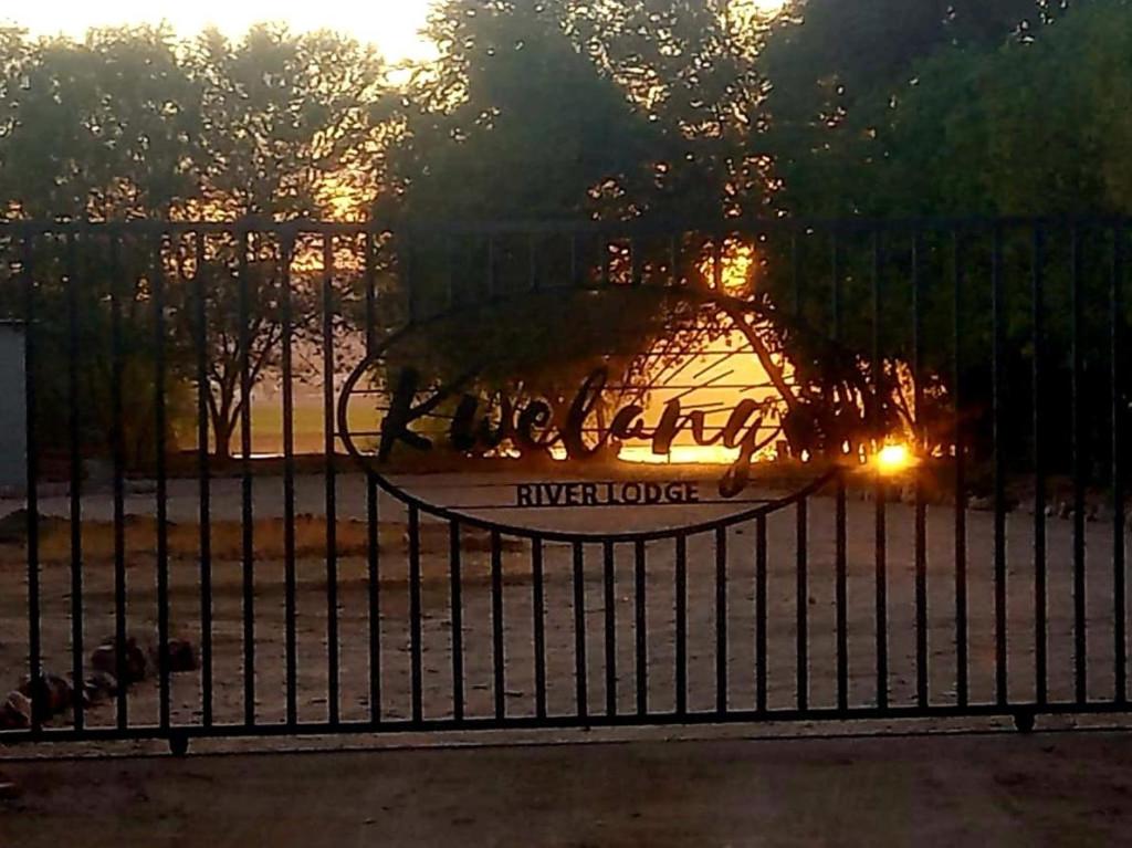 a fence in front of a park with the sunset at Kwelanga River Lodge in Vioolsdrif