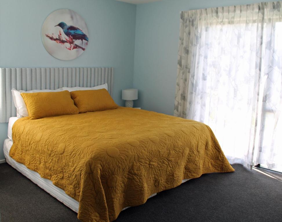 a bedroom with a bed with a yellow blanket and a window at Marlborough Wine Country B&B in Blenheim