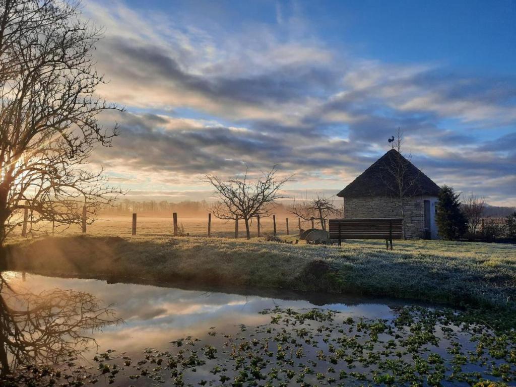 eine Bank und ein Gebäude mit Spiegelung in einem Teich in der Unterkunft Domaine du moulin de Jeanne in Courlaoux