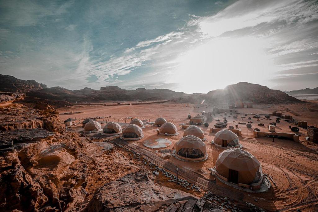 a group of domes in a desert with the sun at Sinam Desert Resort in Wadi Rum