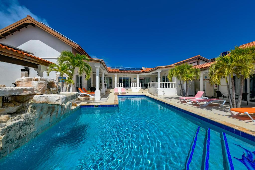 une piscine bordée de palmiers et une maison dans l'établissement Boutique Hotel Swiss Paradise Aruba Villas and Suites, à Palm-Eagle Beach