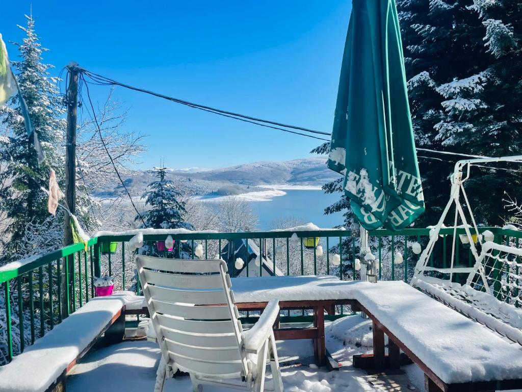 a snowy balcony with a table and chairs and a green umbrella at Ski Hut Gorica Mavrovo in Mavrovo