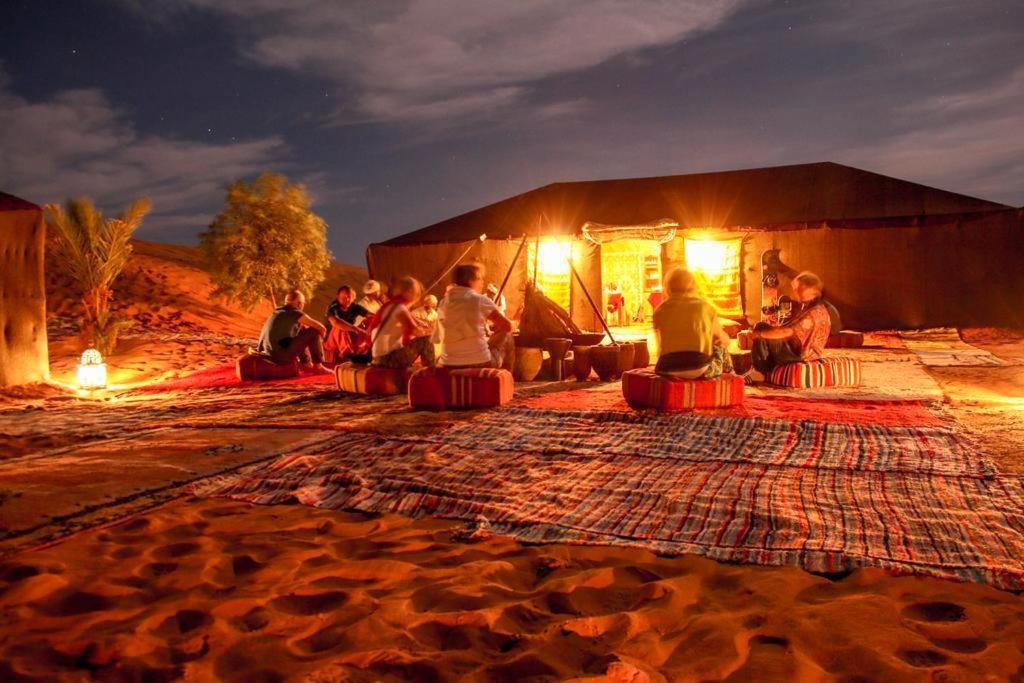 un gruppo di persone seduti di fronte a una tenda di Camp Sahara Majestic a M'Hamid