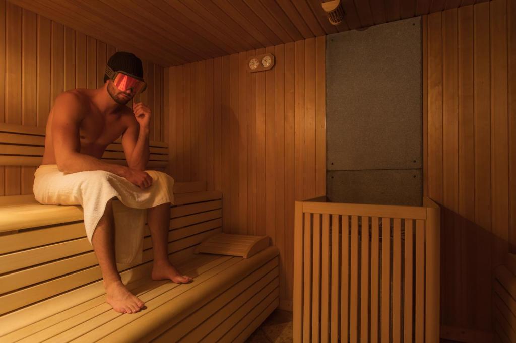 a man sitting in a sauna with a towel at Hotel Chalet Sas Morin in Pozza di Fassa