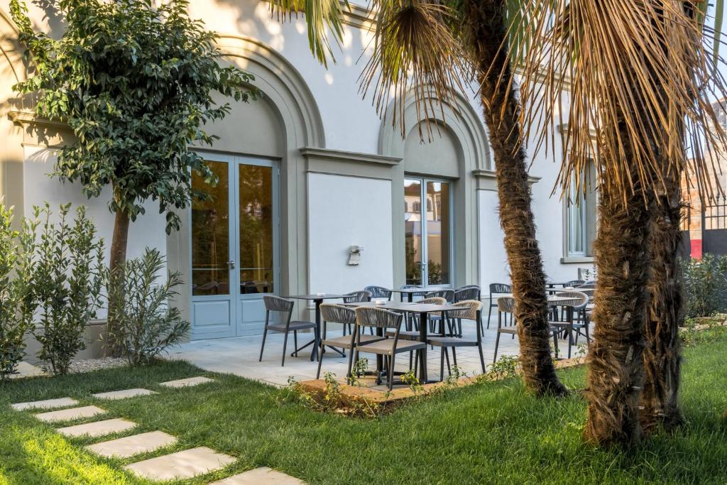 un patio con tavoli, sedie e una palma di Hotel Ariele a Firenze