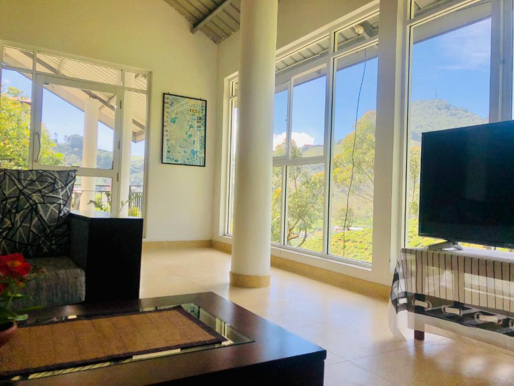 sala de estar con TV y ventanas grandes. en Seeming Lodge, en Nuwara Eliya