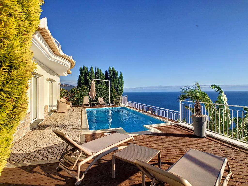 una casa con una piscina con sillas y el océano en Villa Valentina by LovelyStay, en Ponta do Sol