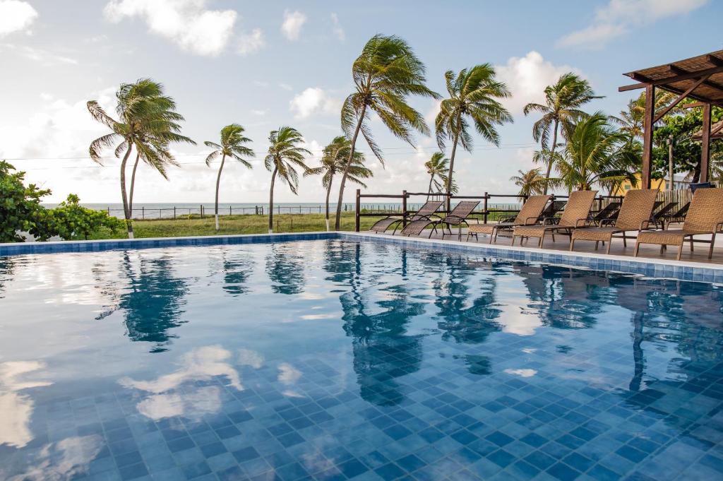 una piscina con sillas y palmeras en Pousada Aldeola by Slaviero Hotéis, en Baixio