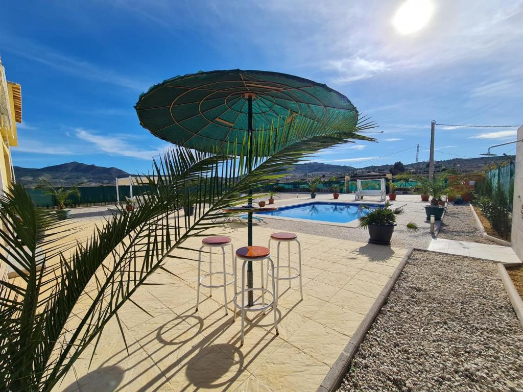 a patio with two stools and an umbrella next to a pool at SUN VILLA in Hondón de los Frailes