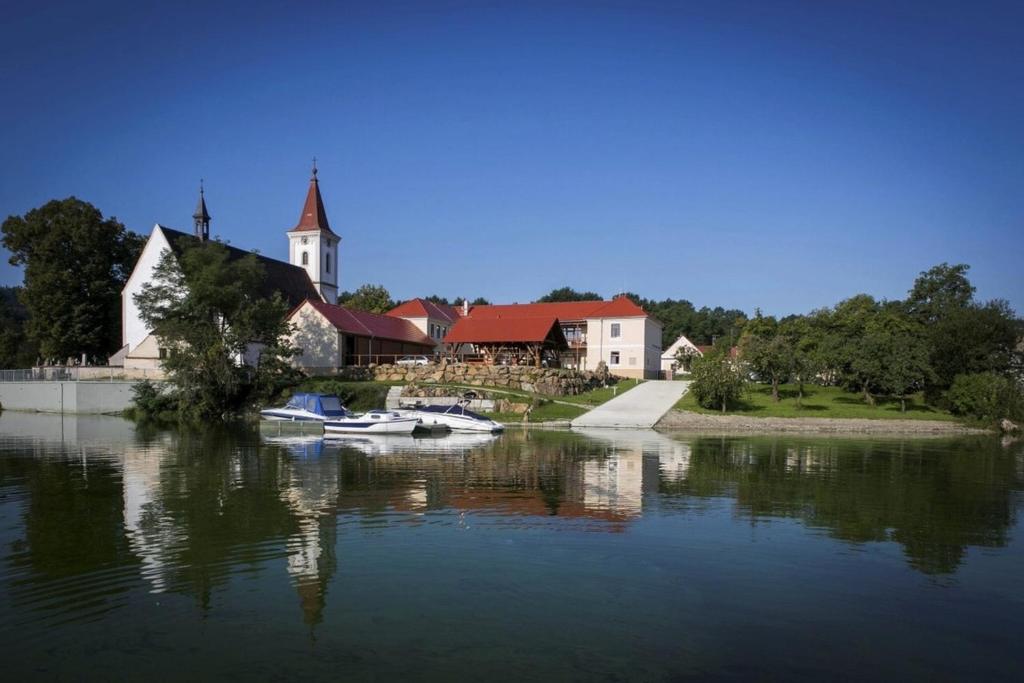 a church and boats in the water in front of a house at Apartmány U Anděla in Purkarec