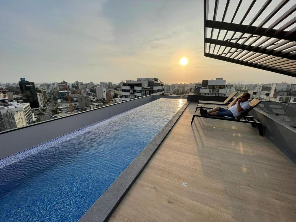 two people sitting on a ledge on a building with a pool at Departamento LOFT COMPLETO in Lima