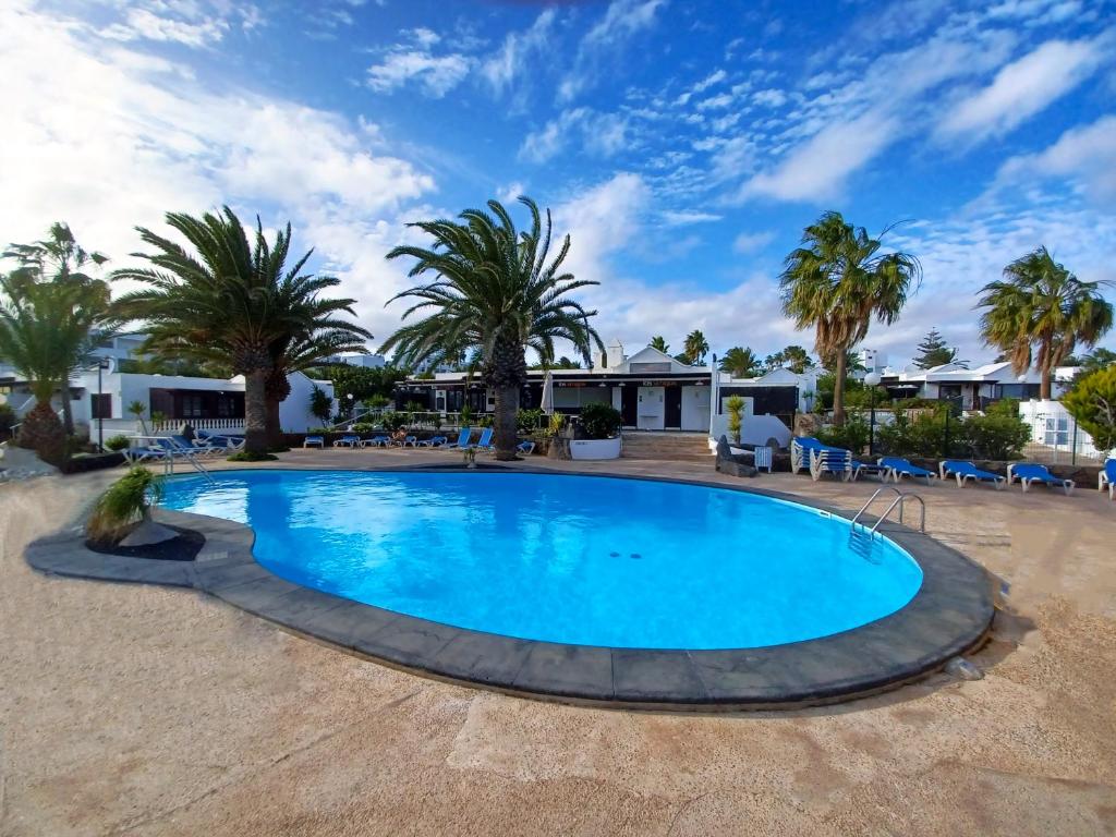 einen Pool in einem Resort mit Palmen in der Unterkunft Bungalow Playa Bastian - Piscina climatizada - Wifi - Playa 1 min. in Costa Teguise