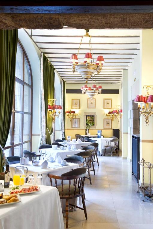 un restaurante con mesas y sillas blancas y ventanas en Parador de Santillana Gil Blas, en Santillana del Mar