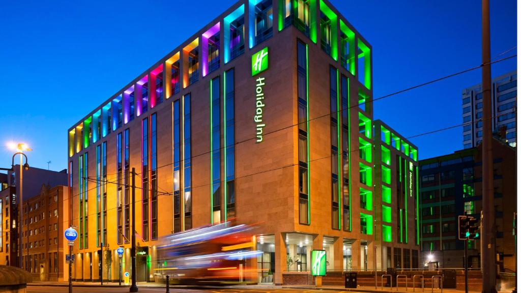 a building with green and colorful lights on it at Holiday Inn Manchester - City Centre by IHG in Manchester