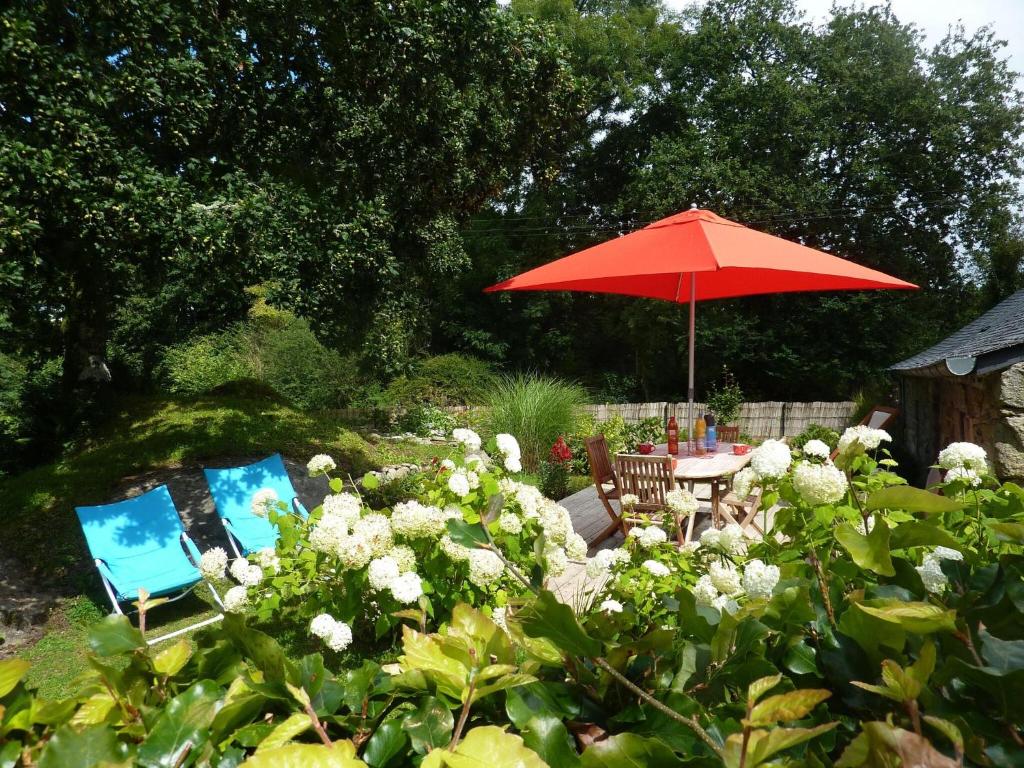 a table and chairs with a red umbrella in a garden at Charming holiday home with garden in Huelgoat