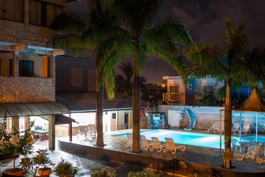 a swimming pool with chairs and palm trees at night at Pousada Pesque Park in Boracéia