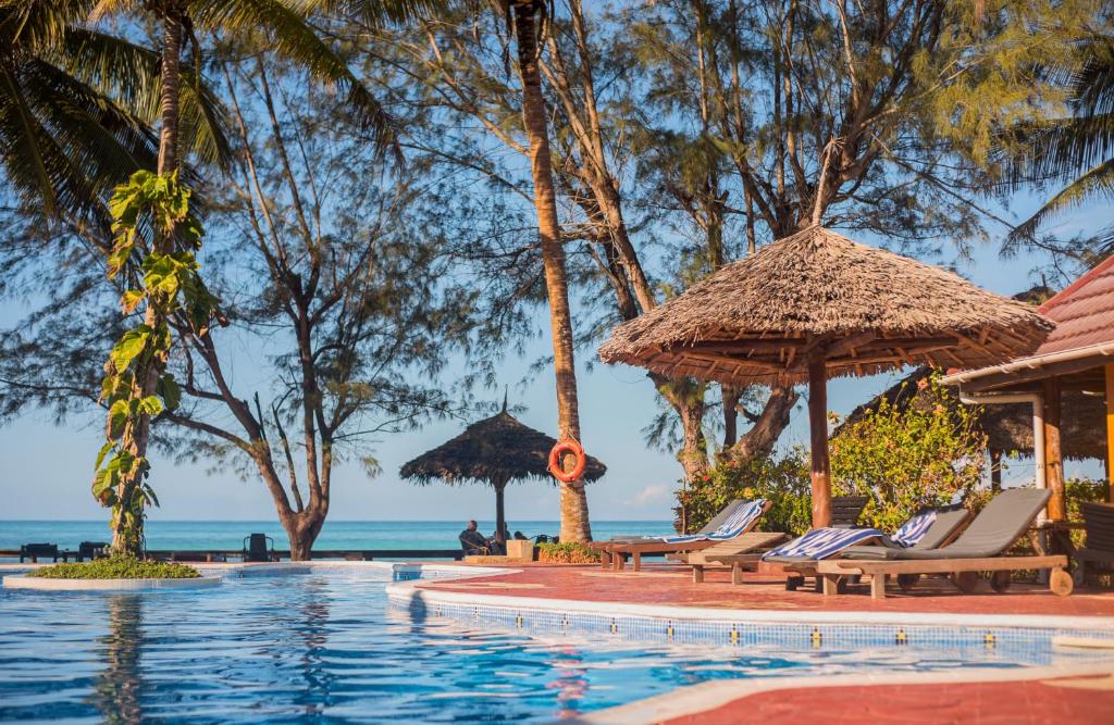 una piscina en un complejo con sillas y sombrillas en Mnarani Beach Cottages, en Nungwi