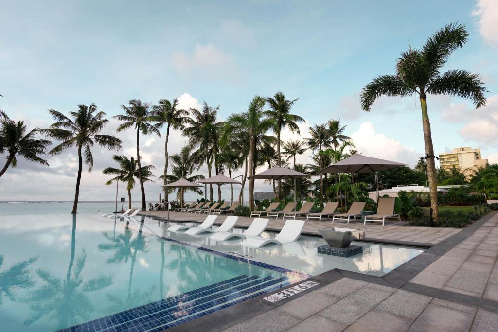 a pool at a resort with chairs and palm trees at Crowne Plaza Resort Guam in Tumon